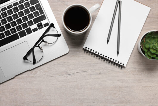 Home office. Laptop, glasses, coffee, houseplant and stationery on white wooden desk, flat lay. Space for text